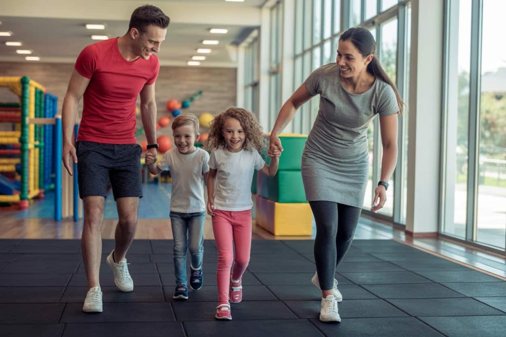 Happy family leaving gym together, kids laughing in play area, parents smiling.