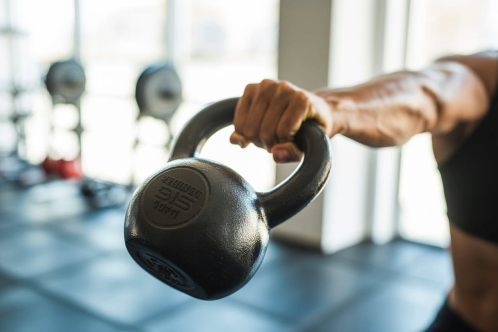 Close-up of a kettlebell mid-swing in a bright, well-lit gym, highlighting motion blur to show dynamic movement.