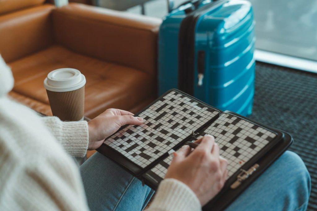 Person solving a crossword puzzle at an airport lounge, coffee and suitcase nearby