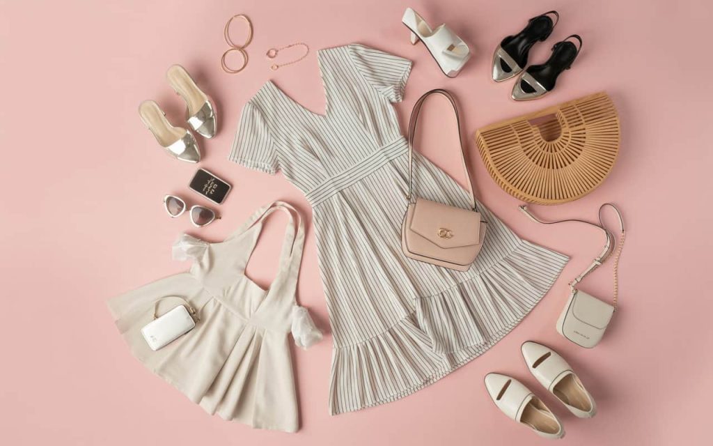 A flat lay of trending women’s outfits, including dresses, bags, shoes, and accessories, pastel-colored background, modern fashion aesthetic.