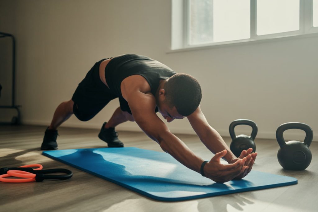 Fitness mat with a person performing dynamic stretches, kettlebells and resistance bands nearby, morning light streaming in.